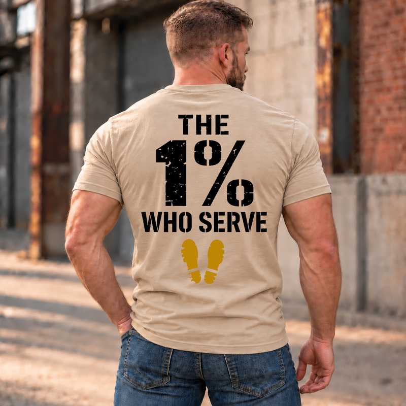 Man wearing a sand The 1% veteran T-shirt, back print view, brick warehouse alley