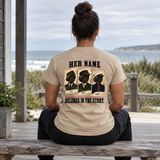 Woman wearing sand colored Her Name Belongs in the Story Marine t-shirt at beach house