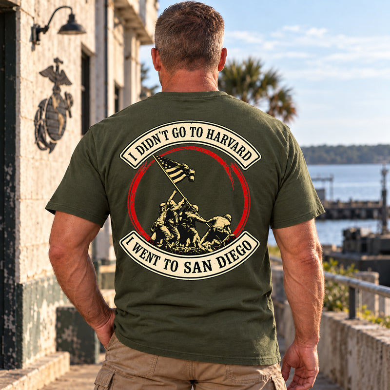 Man wearing a military green San Diego custom year veteran T-shirt, back print view, by the harbor