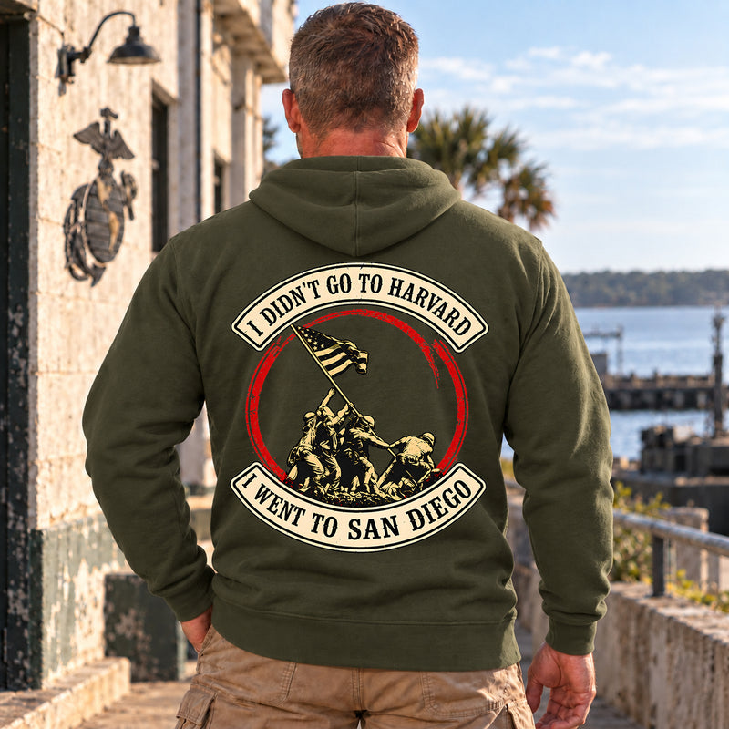 Man wearing a military green San Diego veteran hoodie, back print view, by the harbor