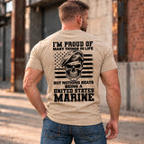 Man wearing a sand Being A Marine custom year veteran T-shirt, back print view, Sunlit industrial street by brick warehouse