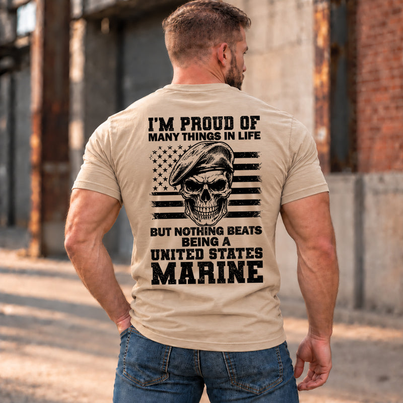 Man wearing a sand Being A Marine custom year veteran T-shirt, back print view, Sunlit industrial street by brick warehouse