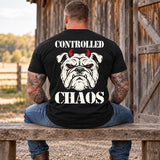 Man wearing a black CONTROLLED CHAOS veteran T-shirt, back print view, wooden bench by a weathered barn