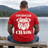 Man wearing a red CONTROLLED CHAOS veteran T-shirt, back print view, lakeside bench below snowy mountains