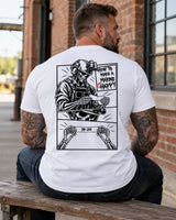 Man wearing a white How to make a marine happy marine veteran T-shirt, back print view, bench by a brick warehouse