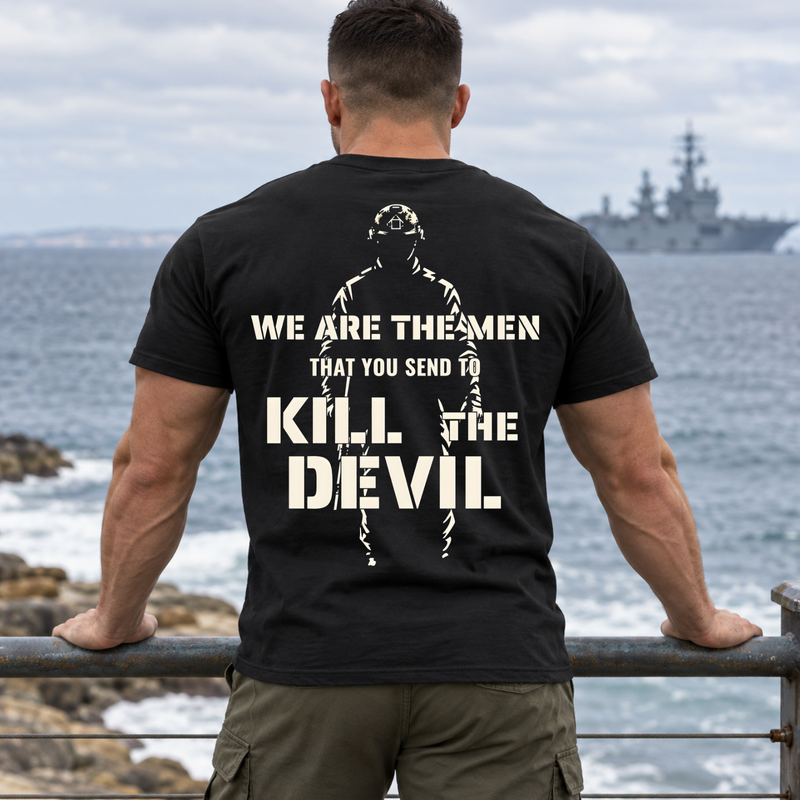 Man wearing a black Kill The Devil custom year veteran T-shirt, back print view, seaside railing with warship offshore