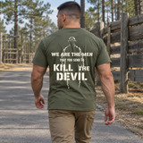 Man wearing a military green Kill The Devil custom year veteran T-shirt, back print view, walking a road past pine trees
