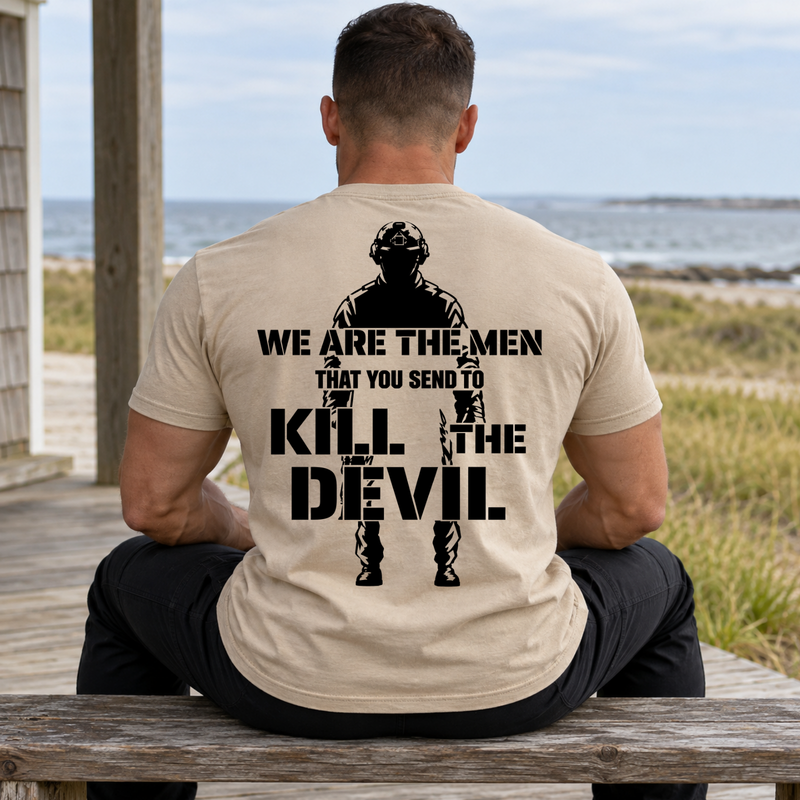 Man wearing a sand Kill The Devil custom year veteran T-shirt, back print view, wooden bench on boardwalk near beach