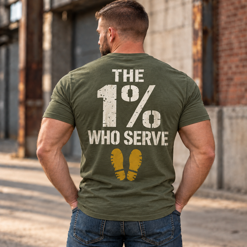 Man wearing a military green The 1% veteran T-shirt, back print view, brick warehouse alley