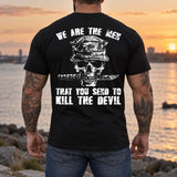 Man wearing a black We are the men veteran T-shirt, back print view, rocky shoreline at sunset