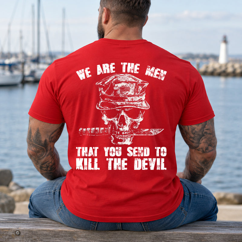 Man wearing a red We are the men veteran T-shirt, back print view, marina bench with a lighthouse beyond