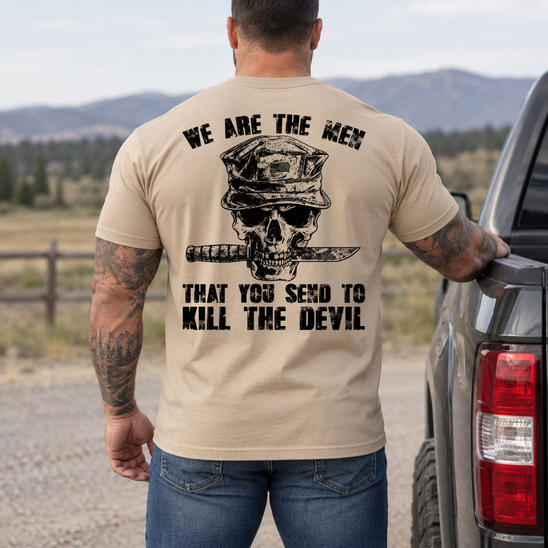 Man wearing a sand We are the men veteran T-shirt, back print view, by a pickup truck near mountain pasture